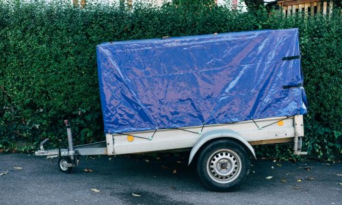 A blue tarpaulin-covered trailer parked on a roadside against a hedge, ideal for transport themes.